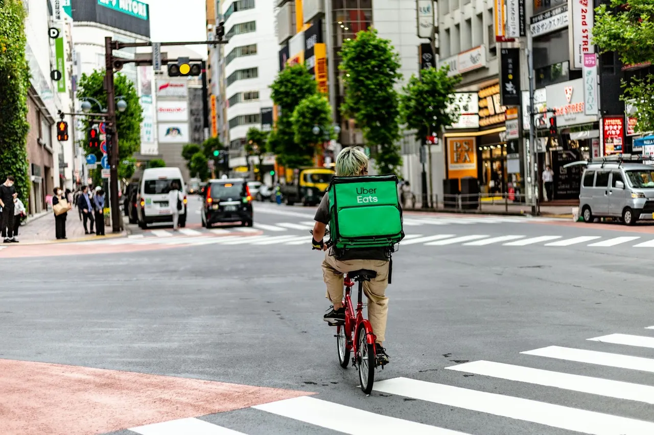 Photo of a hyperlocal delivery rider on a bicycle with an Uber Eats delivery bag, representing the last-mile delivery aspect of quick commerce in an urban environment with heavy foot and vehicle traffic.