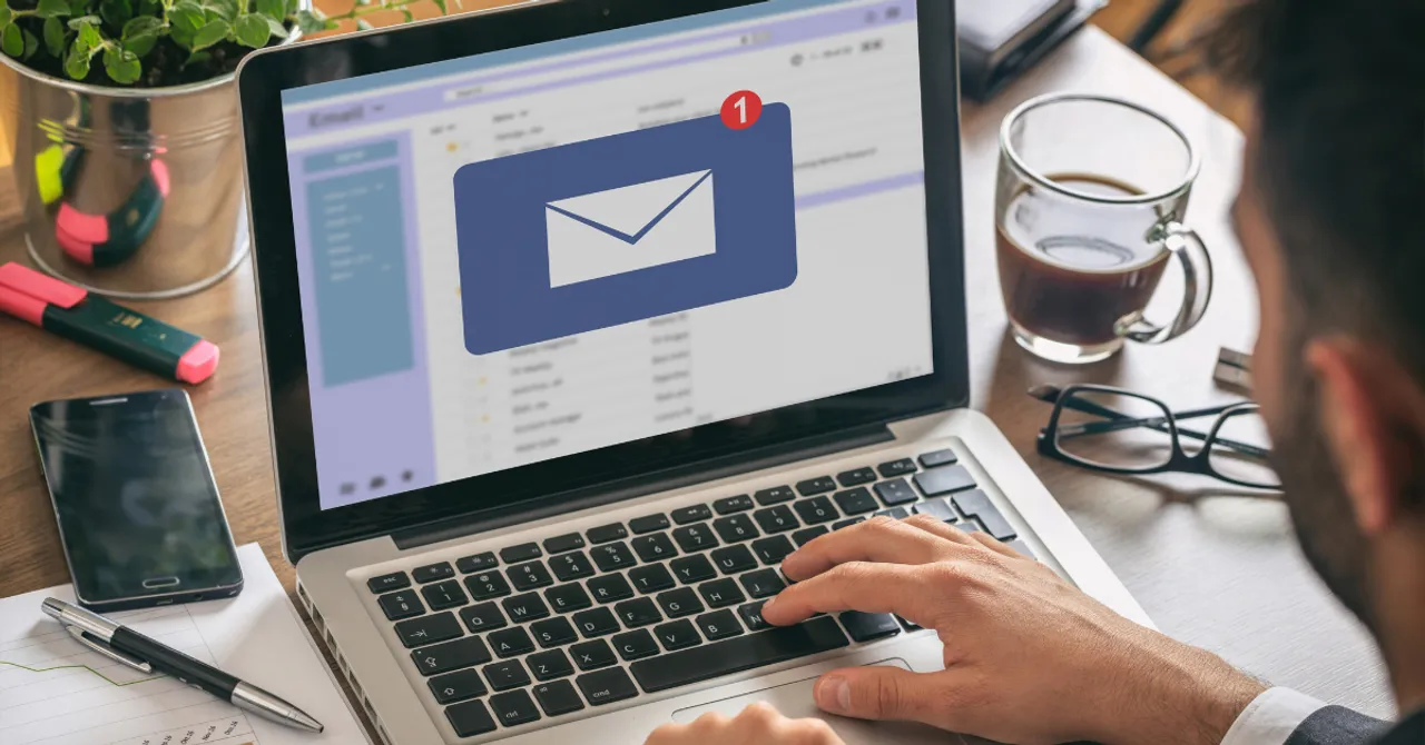 Person checking new email notifications on a laptop at a workspace with coffee and office supplies.