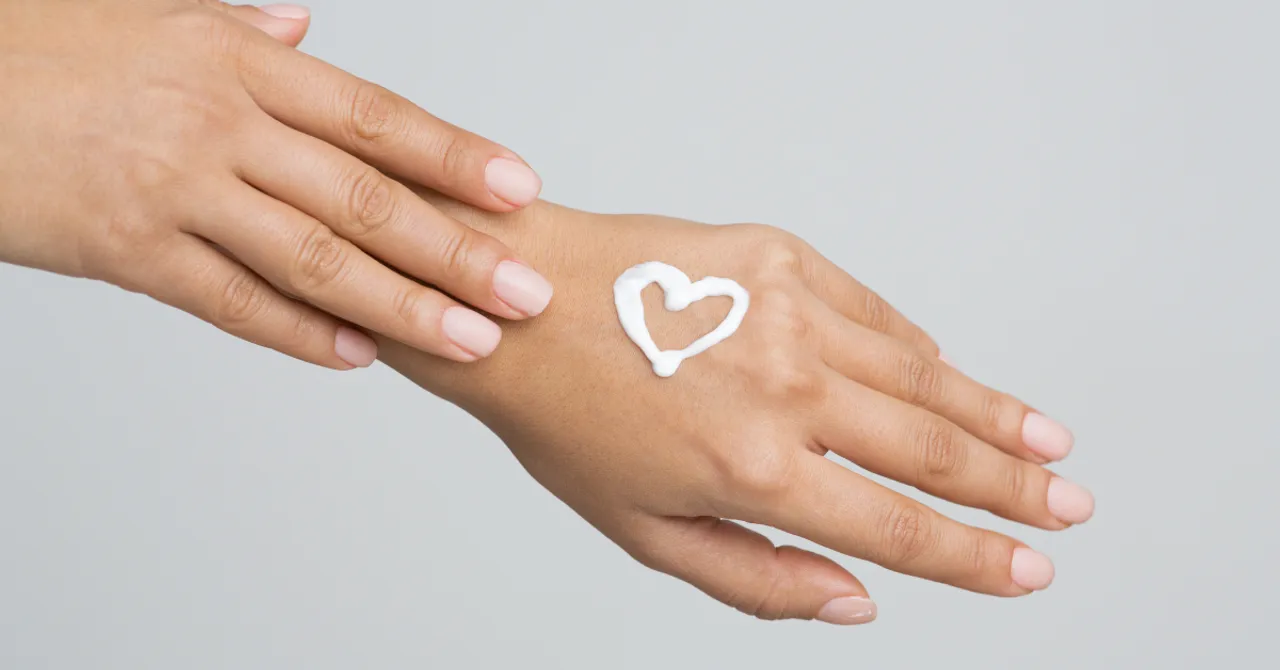 A person gently applying lotion with a heart shape on the back of their hand, symbolizing skincare and self-care.