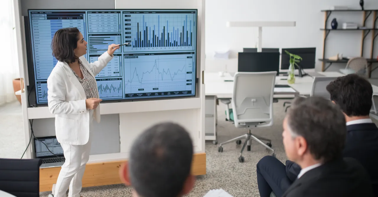 Businesswoman presenting data analytics to a professional team in a modern office.