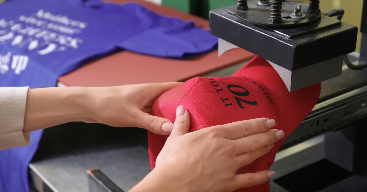 A person custom-printing a red cap using a heat press machine, symbolizing how AI is revolutionizing the print-on-demand process with smart, personalized designs.