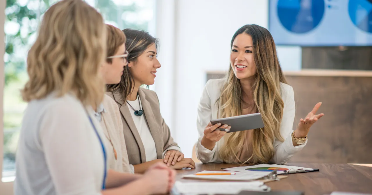 Businesswoman leading a meeting with three colleagues, holding a tablet and discussing a chart.