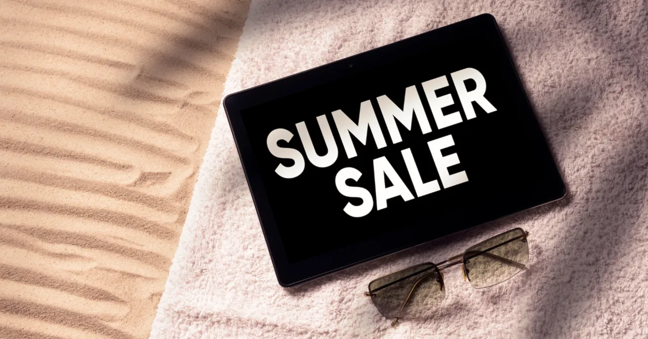 A digital tablet displaying “Summer Sale” on a beach towel beside sunglasses — capturing the vibe of seasonal shopping promotions in a relaxed summer setting.