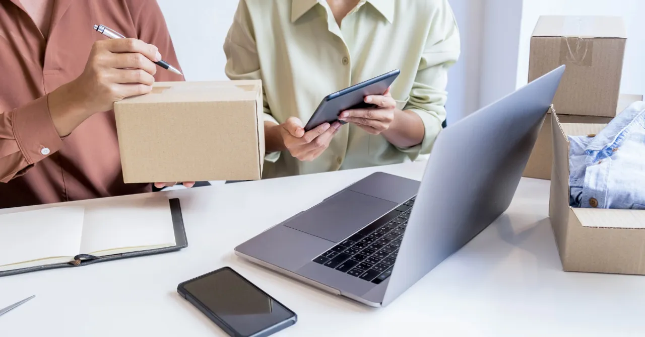 Two small business owners preparing packages for shipping while managing orders on a tablet and laptop — representing the behind-the-scenes of e-commerce operations.