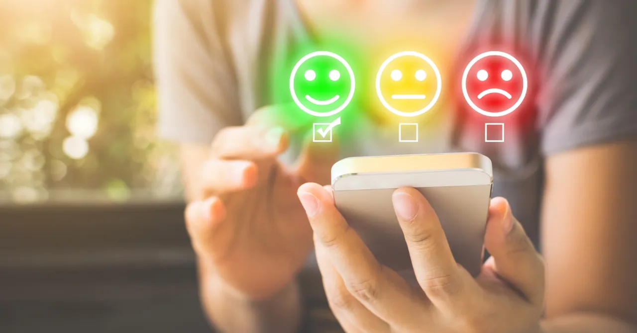 A person using a smartphone to give feedback with emoji faces, highlighting a positive experience through a green smiling face.
