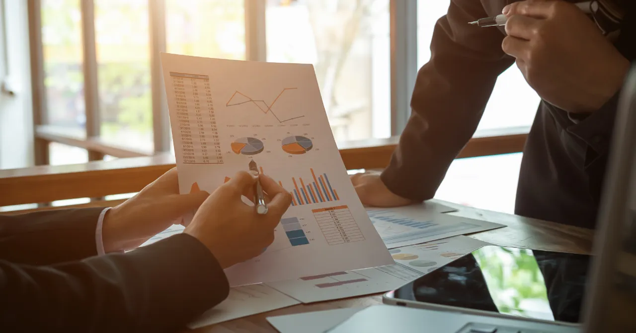 Two people in business attire reviewing printed charts and graphs during a meeting, analyzing data for strategic planning.