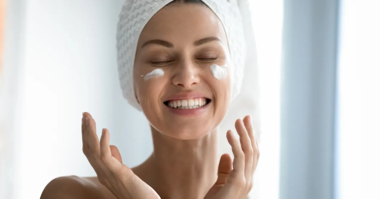 A woman smiling with confidence while applying skincare cream — reflecting the joy of finding the perfect product through AI-powered skin analysis.