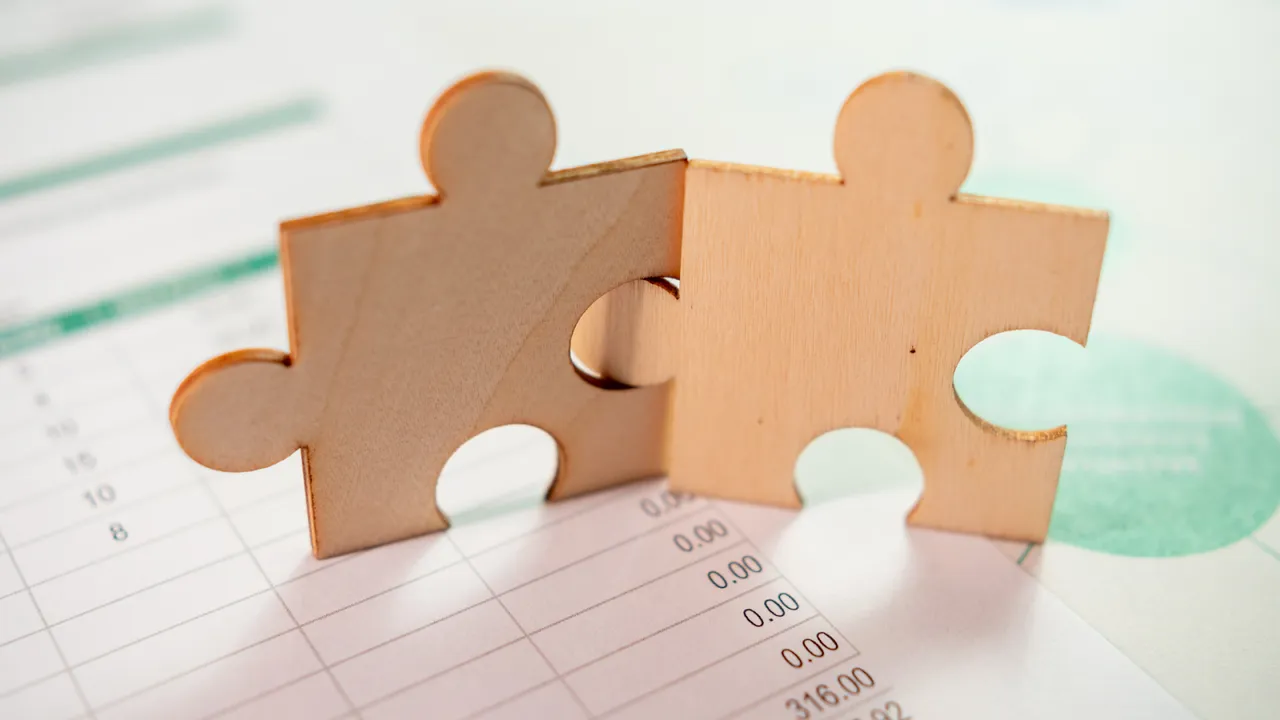 Two wooden puzzle pieces fitting together on top of a financial spreadsheet, symbolizing seamless integration and alignment in business strategy.