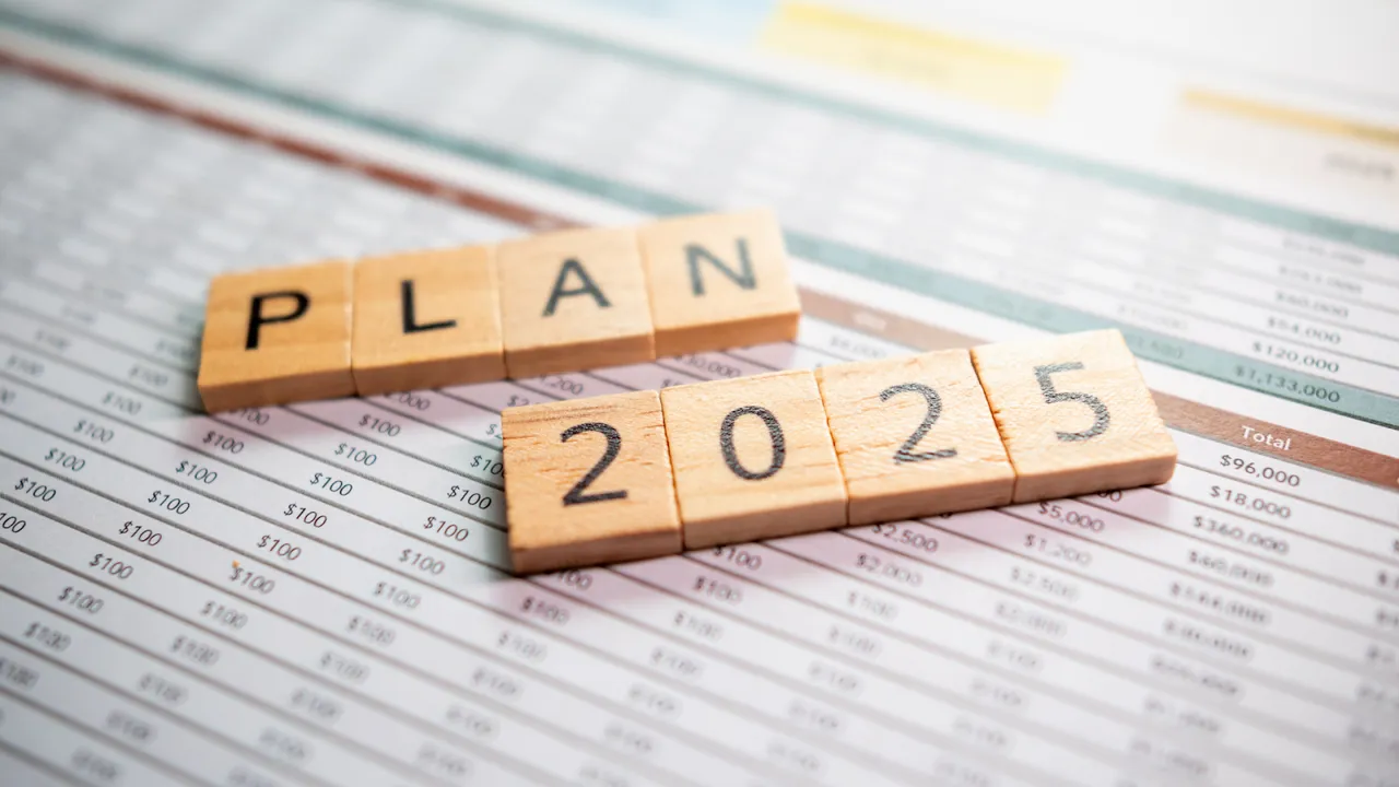 Wooden letter blocks spelling "PLAN 2025" placed on financial spreadsheets, representing strategic business planning for the year 2025